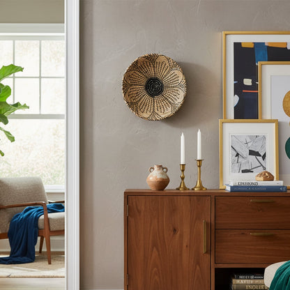 Handcrafted round wall decor in natural woven finish mounted above wooden cabinet adding warm earthy texture to modern living room decor.
