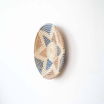 Side angle view of a geometric star pattern woven seagrass wall hanging basket plate showing depth on a white wall.