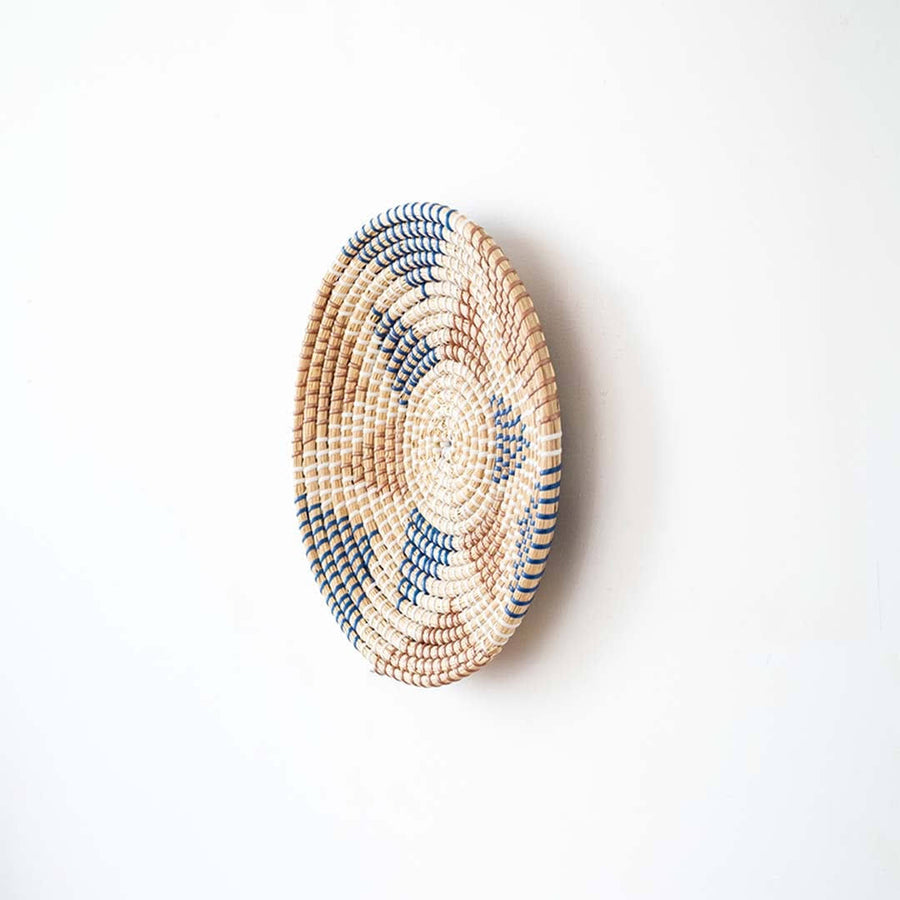 Side angle view of a geometric star pattern woven seagrass wall hanging basket plate showing depth on a white wall.