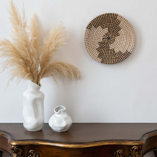 Handwoven wall basket decor in natural and black fiber styled above console table with vases for boho wall.