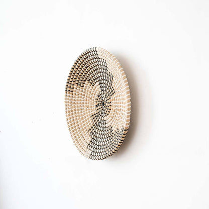 Side angle view of a spiral pattern black woven seagrass wall hanging basket plate showing depth on a white wall.