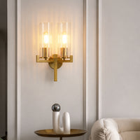 Luxury gold brass double candle wall sconce fixture illuminated beautifully against a white paneled living room wall.
