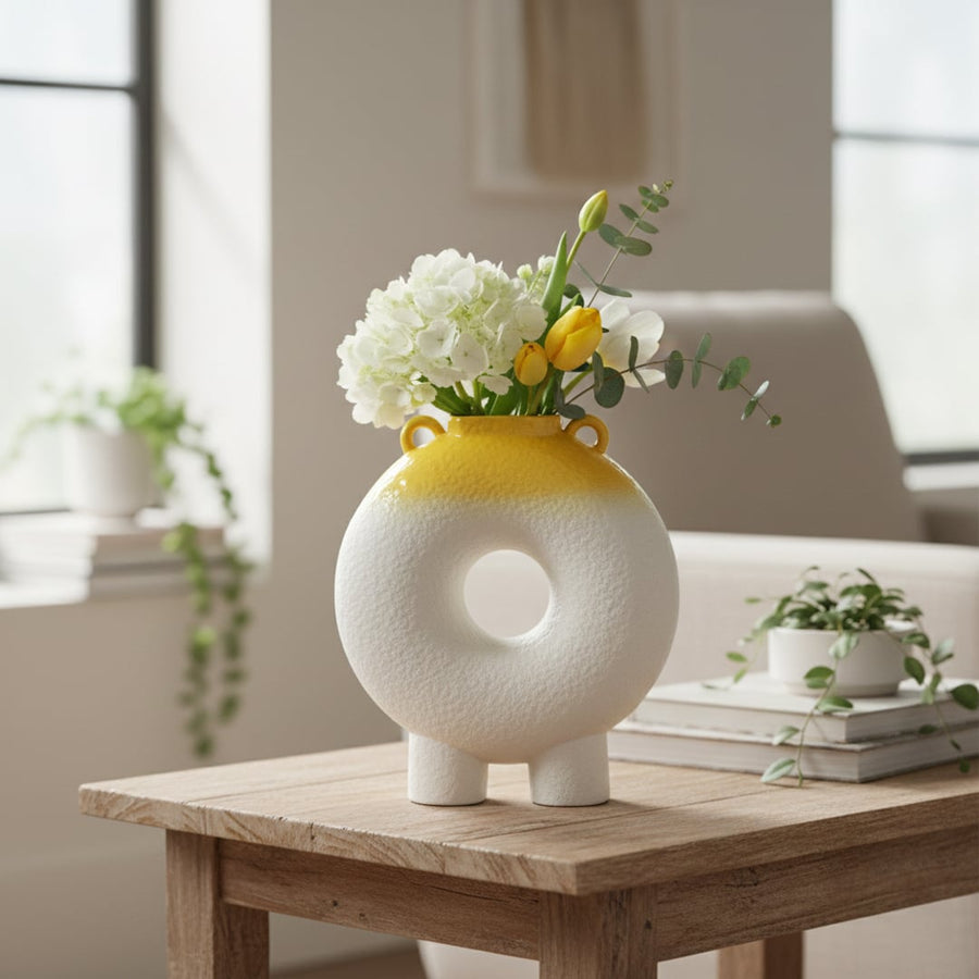 White and yellow textured ceramic decorative ring vase styled with fresh flowers on wooden table in bright modern living room.