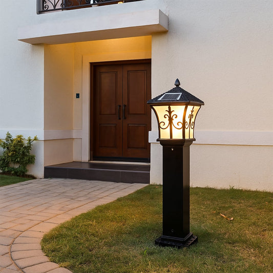 Outdoor pillar lamp with black metal body and glass panels installed near entrance creating warm welcoming exterior lighting for home pathways.