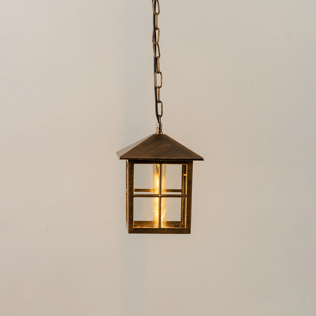 Gold metal hanging outdoor lantern with square glass enclosure glowing on white background suitable for porch entrance and exterior decor lighting.