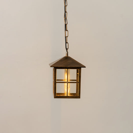 Gold metal hanging outdoor lantern with square glass enclosure glowing on white background suitable for porch entrance and exterior decor lighting.