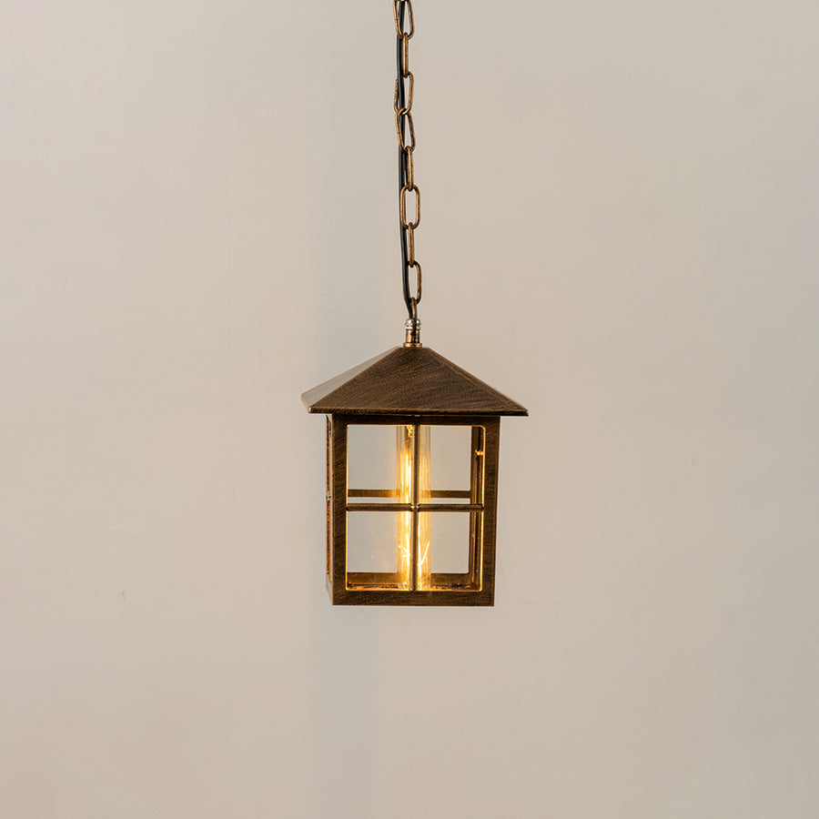 Gold metal hanging outdoor lantern with square glass enclosure glowing on white background suitable for porch entrance and exterior decor lighting.