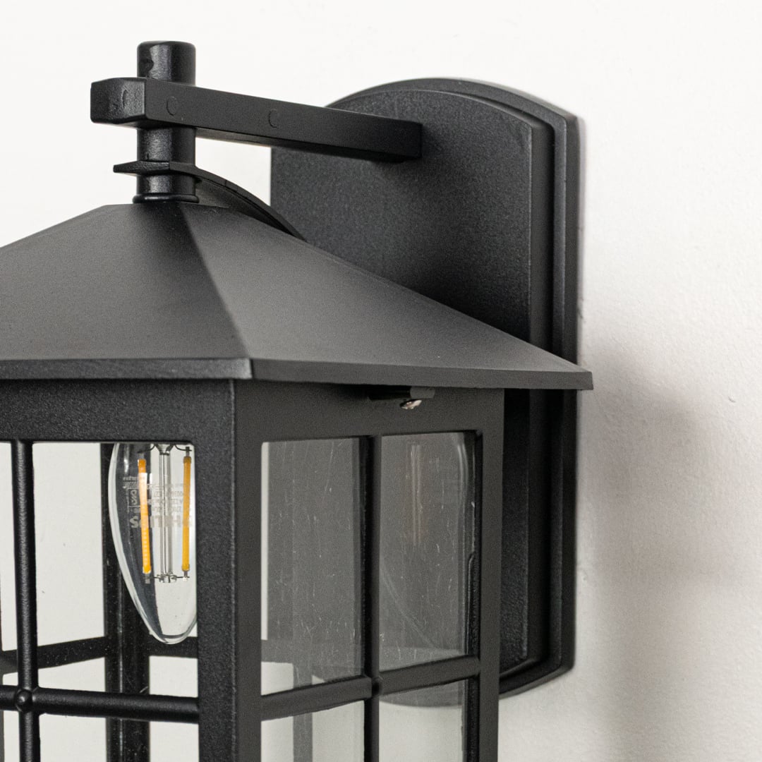 Closeup view of black metal wall lantern highlighting clear glass panels square frame and durable outdoor construction.