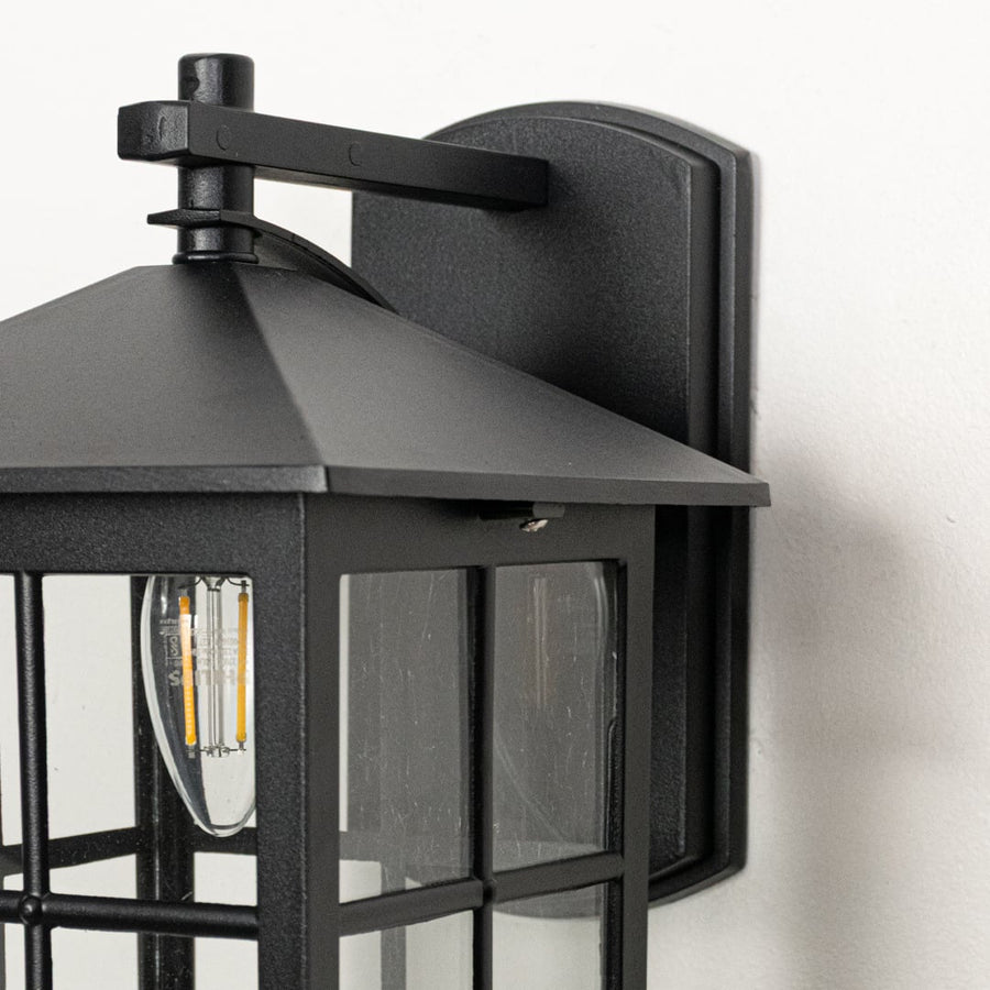 Closeup view of black metal wall lantern highlighting clear glass panels square frame and durable outdoor construction.