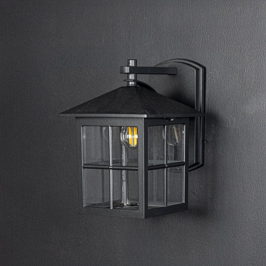 Outdoor black metal wall lantern switched off on dark background emphasizing clean lines square shape and sturdy build.