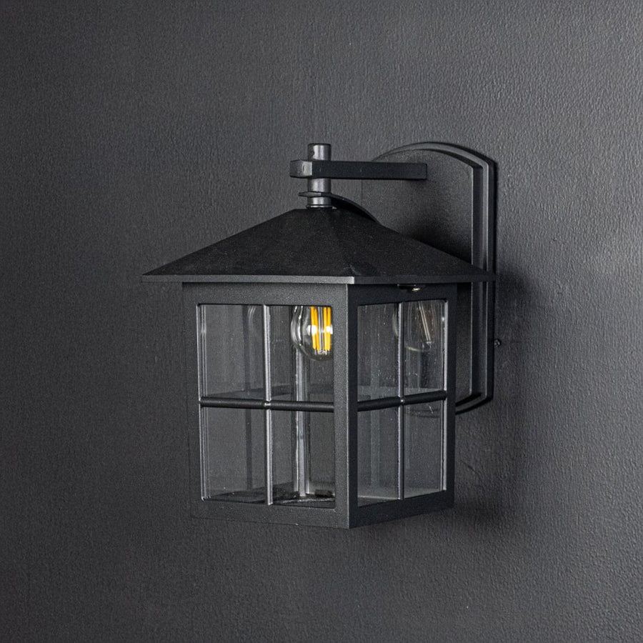 Outdoor black metal wall lantern switched off on dark background emphasizing clean lines square shape and sturdy build.