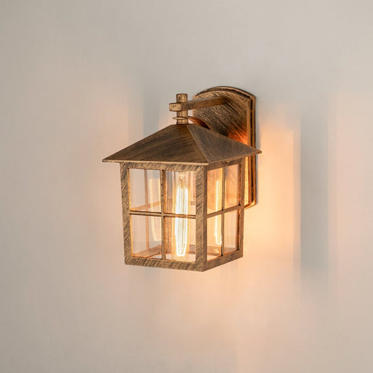Antique brass outdoor wall lantern on white background with windowpane clear glass shade casting a warm porch glow.