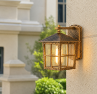 Vintage brass metal grid square wall lantern fixture on beige stucco pillar for rustic farmhouse patio exterior lighting.