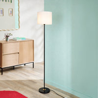 Black metal floor lamp with white fabric drum shade styled beside a cabinet in a modern contemporary living space.