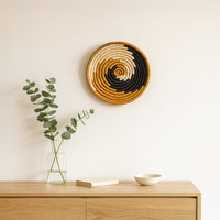 Spiral patterned woven wall basket displayed above sideboard with glass vase creating artistic statement for modern interior Decor.