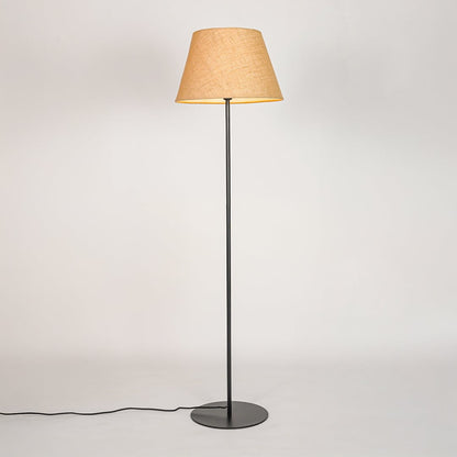 Black standing floor lamp illuminated through beige fabric shade casting soft warm glow on white backdrop.