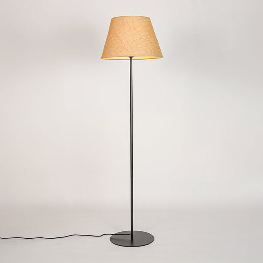 Black standing floor lamp illuminated through beige fabric shade casting soft warm glow on white backdrop.