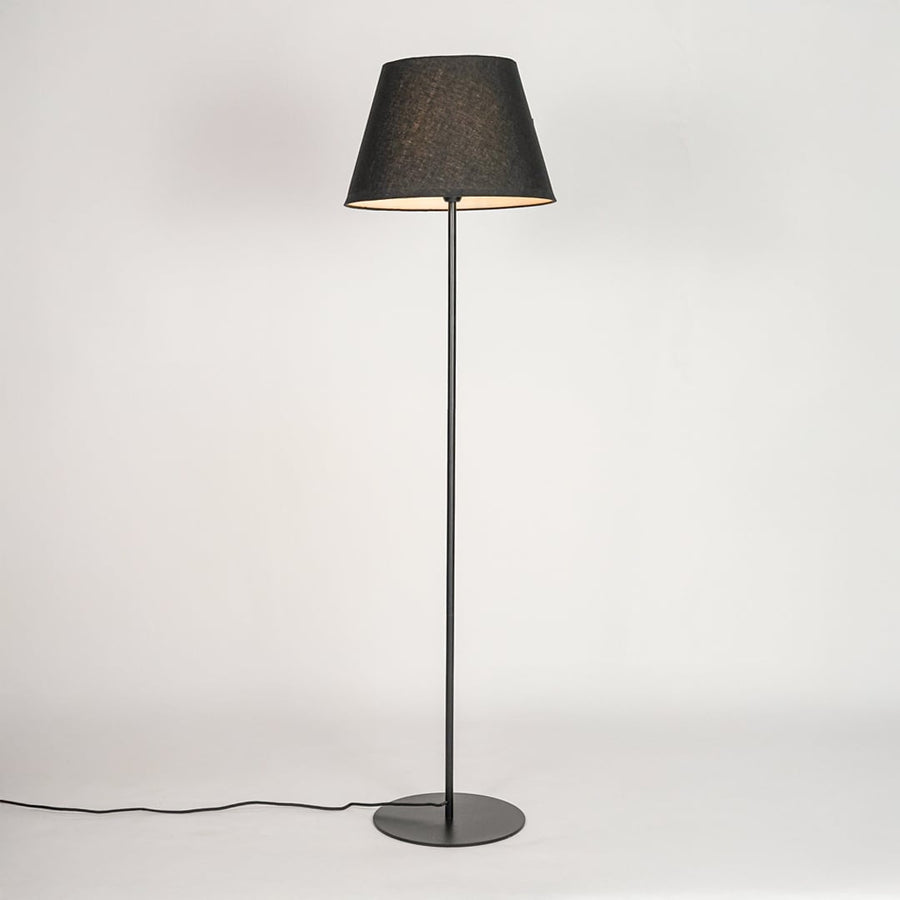 Black floor lamp illuminated through dark grey shade casting soft warm glow against white backdrop.