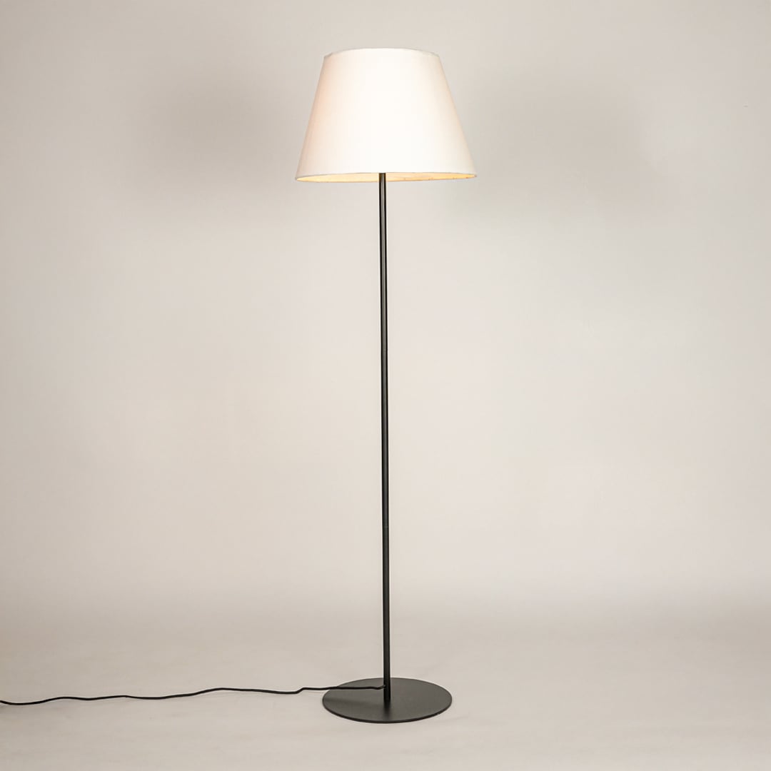 Black metal floor lamp glowing warmly through white fabric shade on white background for cozy home Decor.