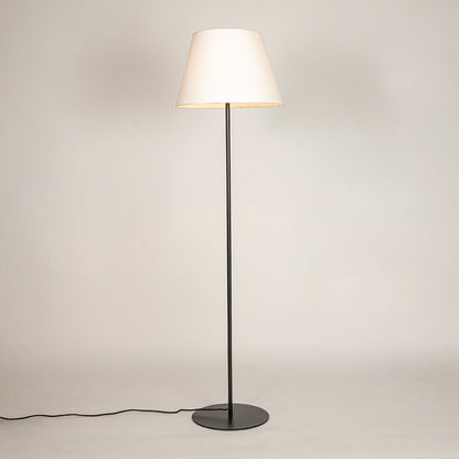 Black metal floor lamp glowing warmly through white fabric shade on white background for cozy home Decor.
