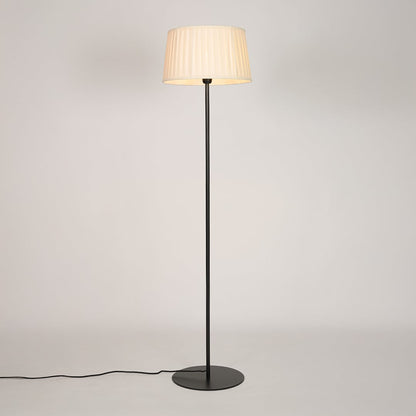 Black metal floor lamp glowing warmly through pleated cream fabric shade on white background for cozy home Decor.