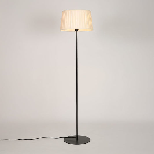 Black metal floor lamp glowing warmly through pleated cream fabric shade on white background for cozy home Decor.