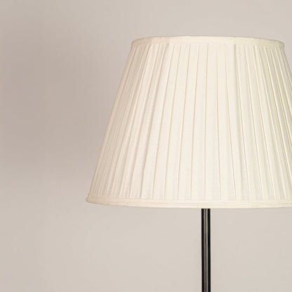 Tapered pleated cream fabric lampshade designed to softly diffuse light and create warm inviting illumination.