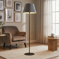 Modern black metal floor lamp with grey velvet shade styled in minimal contemporary living room corner setting.
