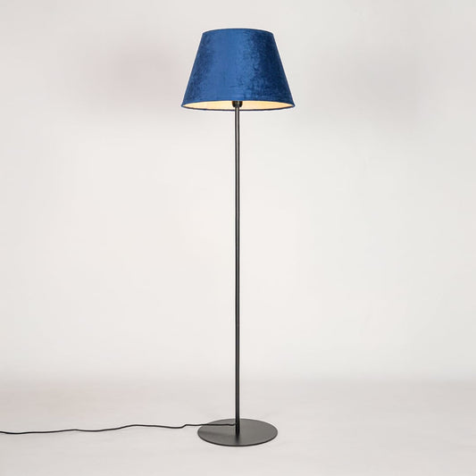 Black floor lamp illuminated through blue fabric shade casting soft diffused glow on white backdrop.