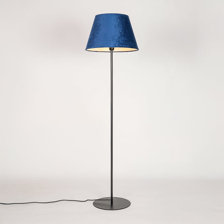Black floor lamp illuminated through blue fabric shade casting soft diffused glow on white backdrop.