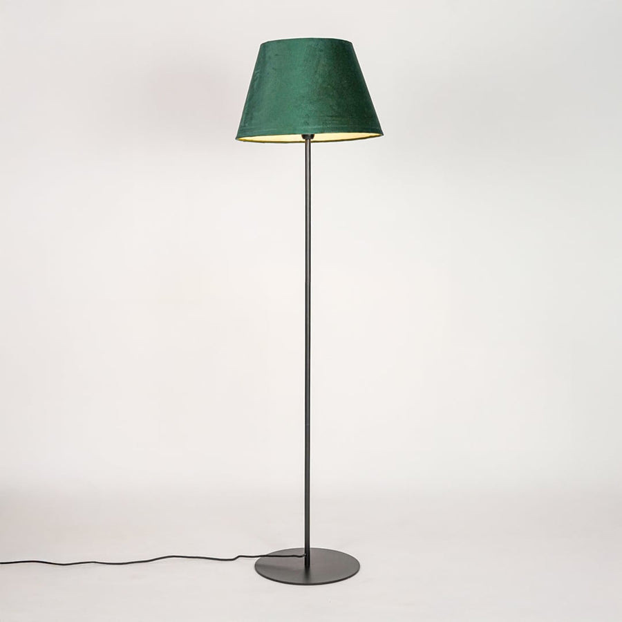 Black floor lamp illuminated through green velvet shade casting soft diffused glow on white backdrop.