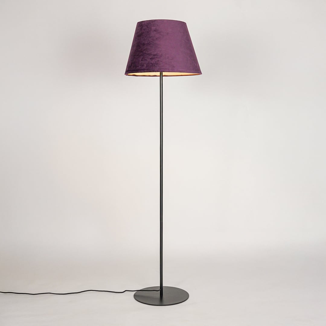 Black floor lamp illuminated through purple fabric shade creating cozy warm glow against white backdrop.