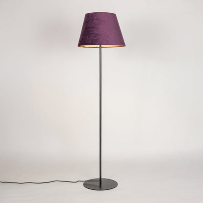 Black floor lamp illuminated through purple fabric shade creating cozy warm glow against white backdrop.