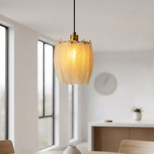A modern pendant light with a textured, leaf-like translucent shade glowing with warm light, hanging in a bright, minimalist dining room.