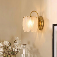 Luxury brass metal curved arm frosted glass petal wall sconce casting warm light in a corner above white flowers for elegant home decor.