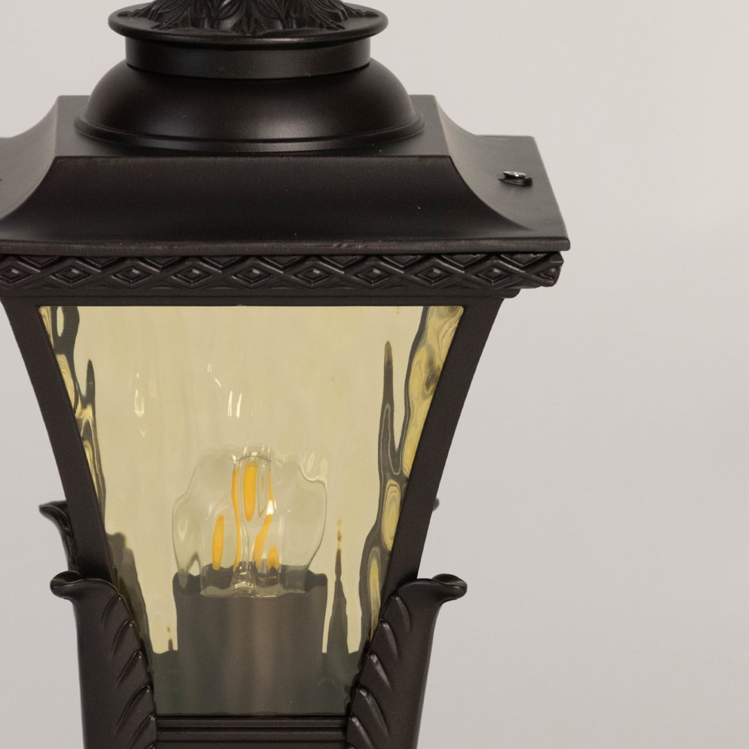 Detailed closeup of outdoor black pillar lamp with textured amber glass shade and ornate classic vintage design.