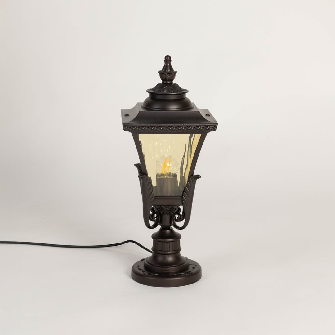 Traditional outdoor pillar lamp in matte black finish with decorative amber glass shade for entrance and balcony use.