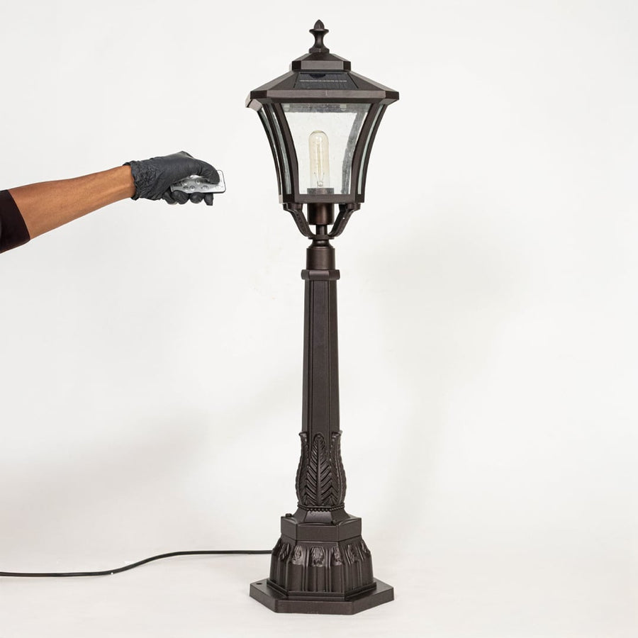 Tall solar pillar lamp post with black frame and clear glass displayed off on plain white background.