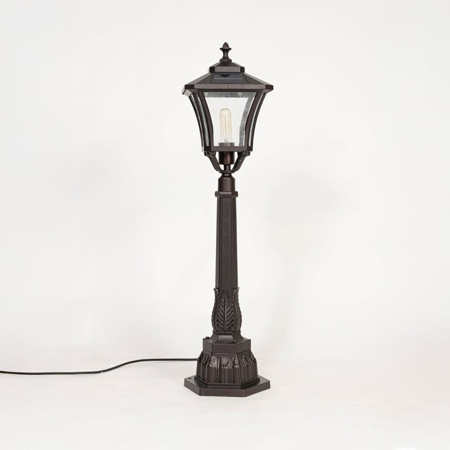 Solar pillar light with black metal frame and glass shade shown off on white background highlighting classic design.