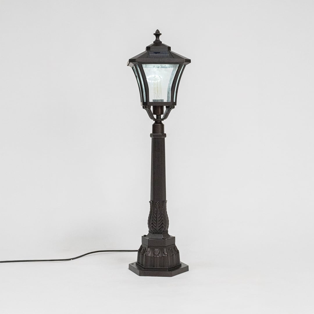 Stylish solar pillar lamp post glowing softly through clear glass shade ideal for modern outdoor garden lighting.
