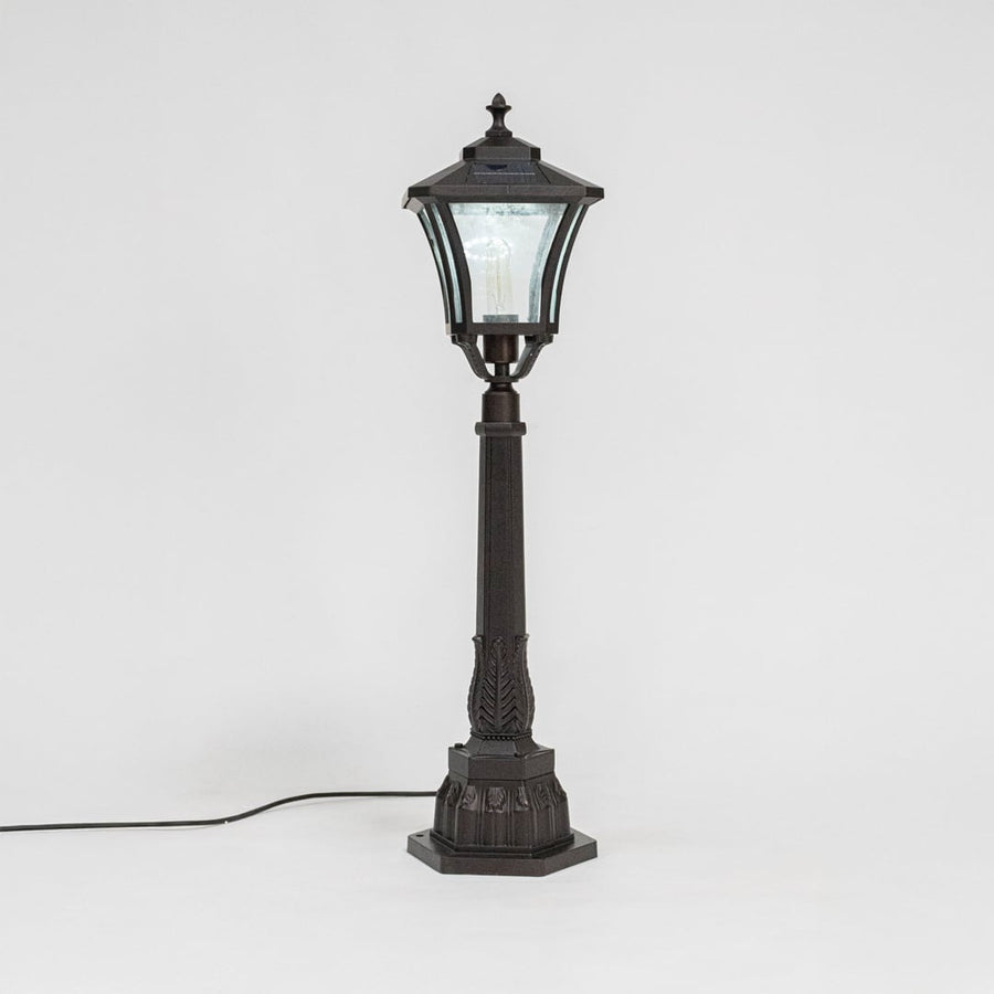 Stylish solar pillar lamp post glowing softly through clear glass shade ideal for modern outdoor garden lighting.