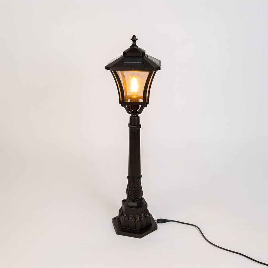 Outdoor post lamp in black metal with glass panels displayed on white background showcasing traditional garden lighting style.