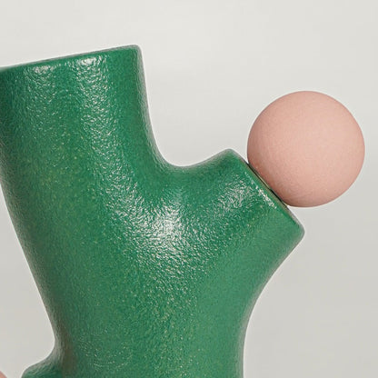 Closeup of glossy green ceramic vase with blush pink ball details showcasing artistic contemporary home decor styling.