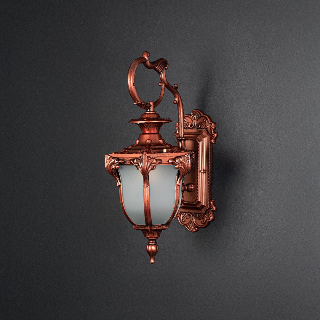Outdoor wall light with antique bronze finish and frosted glass shade glowing warmly off black background.