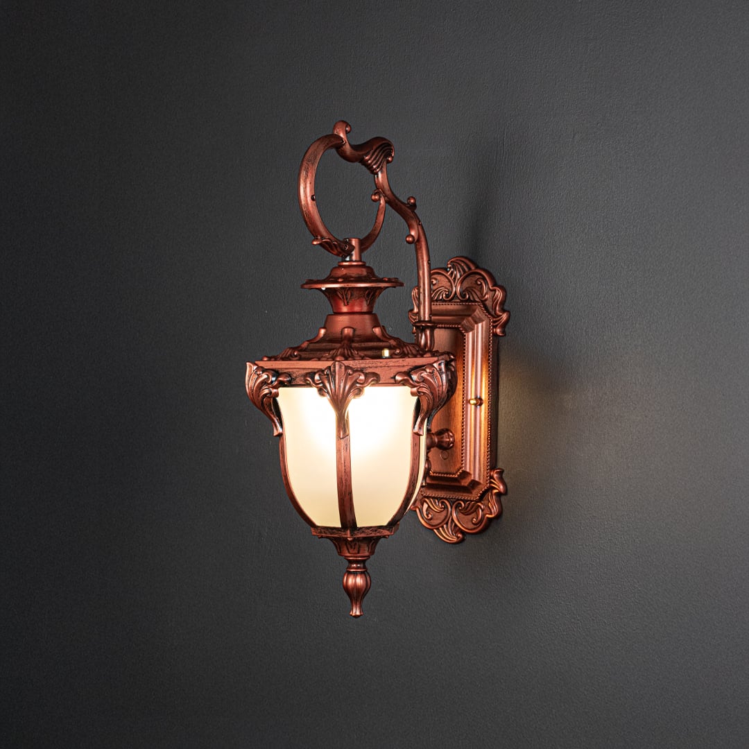 Outdoor wall light with antique bronze finish and frosted glass shade glowing warmly on black background.