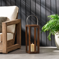 Rustic brown wooden lantern frame housing a glowing candle placed on an outdoor patio floor near a cozy garden armchair.