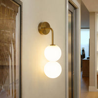 Gold wall light with double white glass globes installed in interior space warm ambient lighting ideal for bedroom and hallway decor.