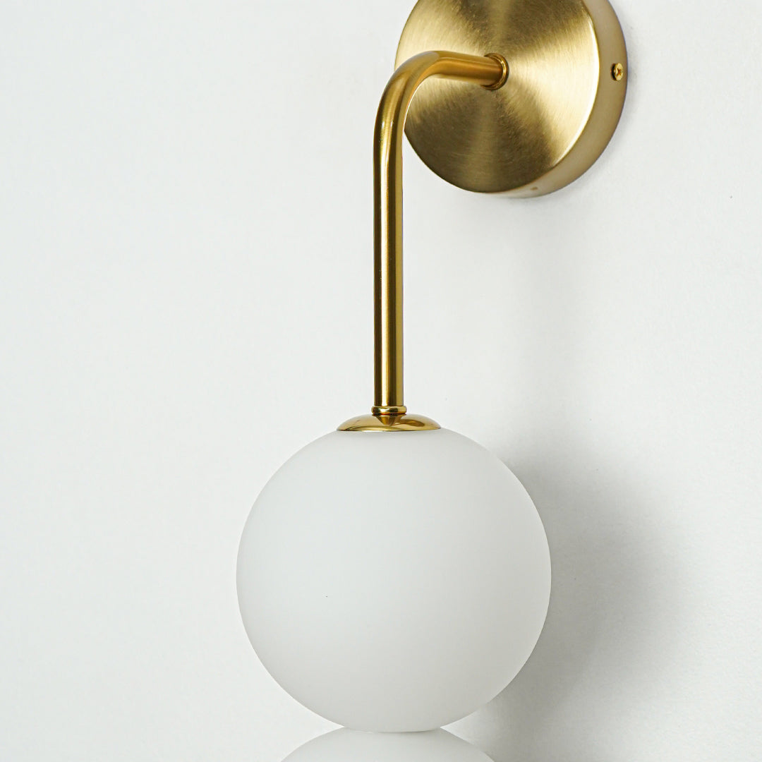 Close up wall light with gold mount and white glass globe on neutral background minimal modern lighting for home decor.