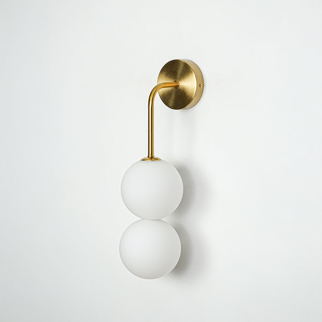 Gold wall light with dual white frosted glass globes on white background modern vertical lighting ideal for bedroom and living room decor.