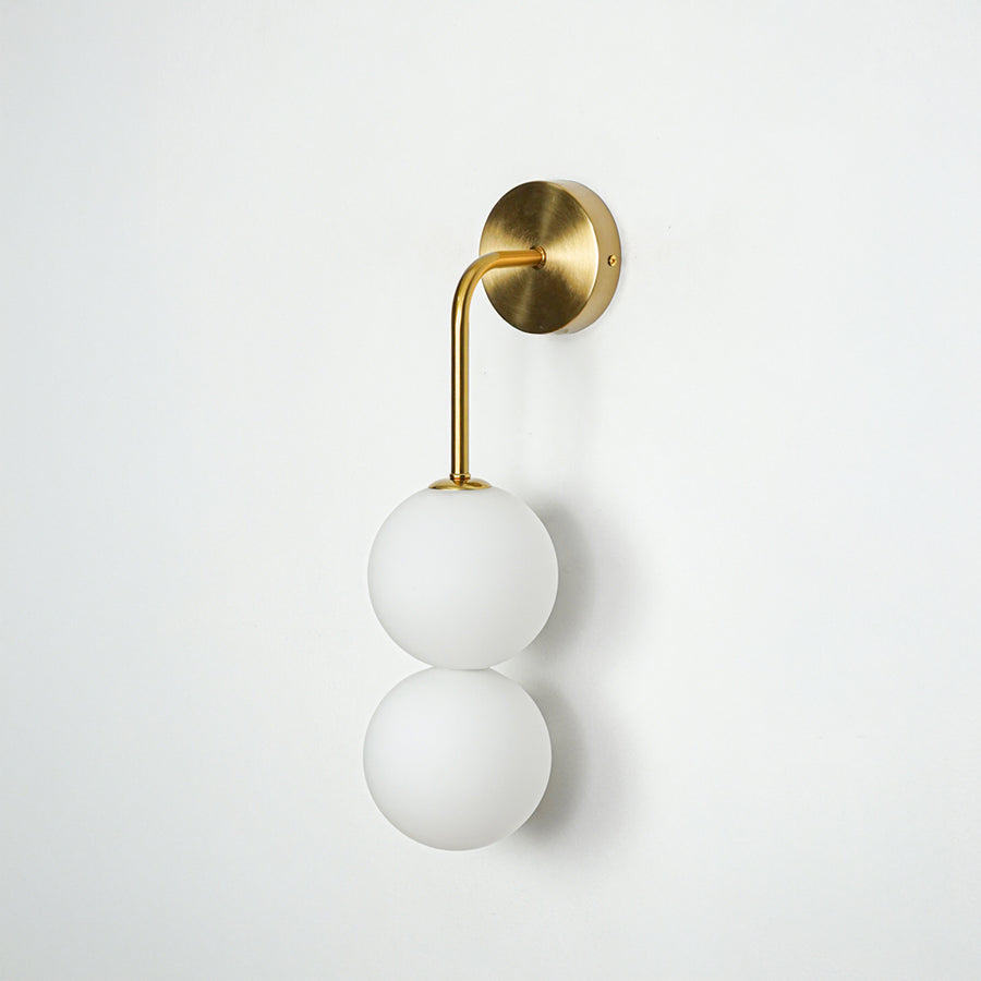 Gold wall light with dual white frosted glass globes on white background modern vertical lighting ideal for bedroom and living room decor.